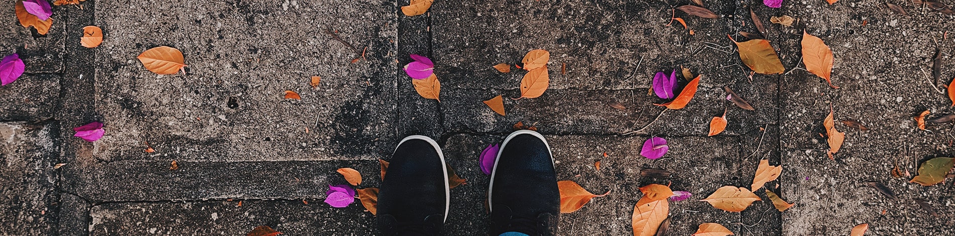 Person in tennis shoes standing on a sidewalk with leaves