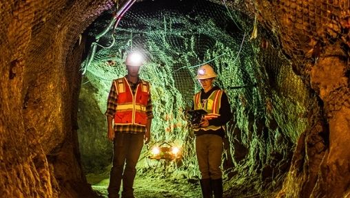 two people are standing in a cave with hard hats and neon orange vests on.